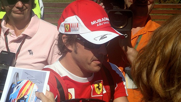 Fernando Alonso takes a moment to sign autographs before heading to the paddock